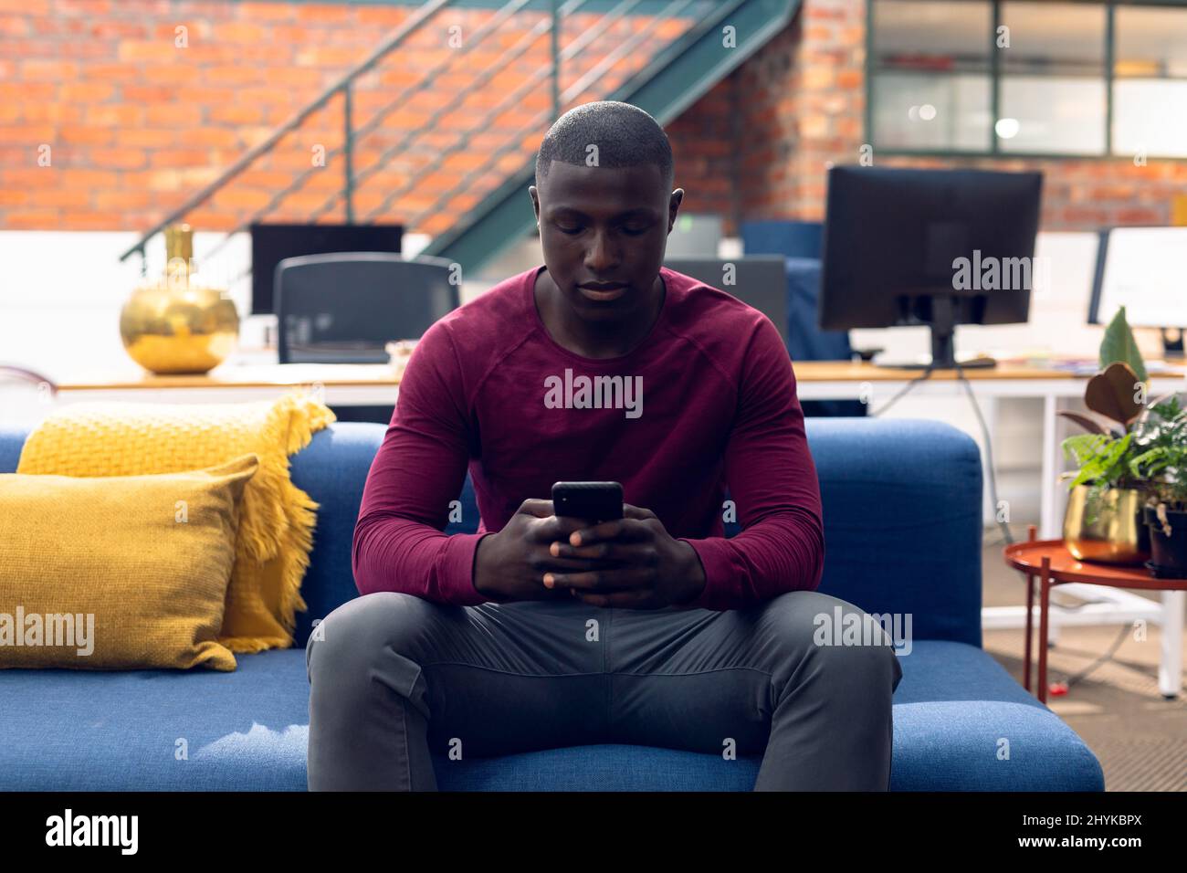 Giovane uomo d'affari afroamericano che usa lo smartphone mentre si siede sul divano in un ufficio moderno Foto Stock