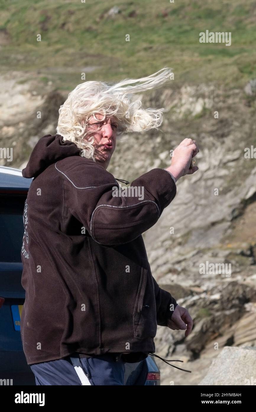 Un uomo che usa un telefono cellulare per registrare il tempo selvaggio e il forte vento che gli soffia i capelli intorno al viso portato da Storm Eunice a Newquay Foto Stock