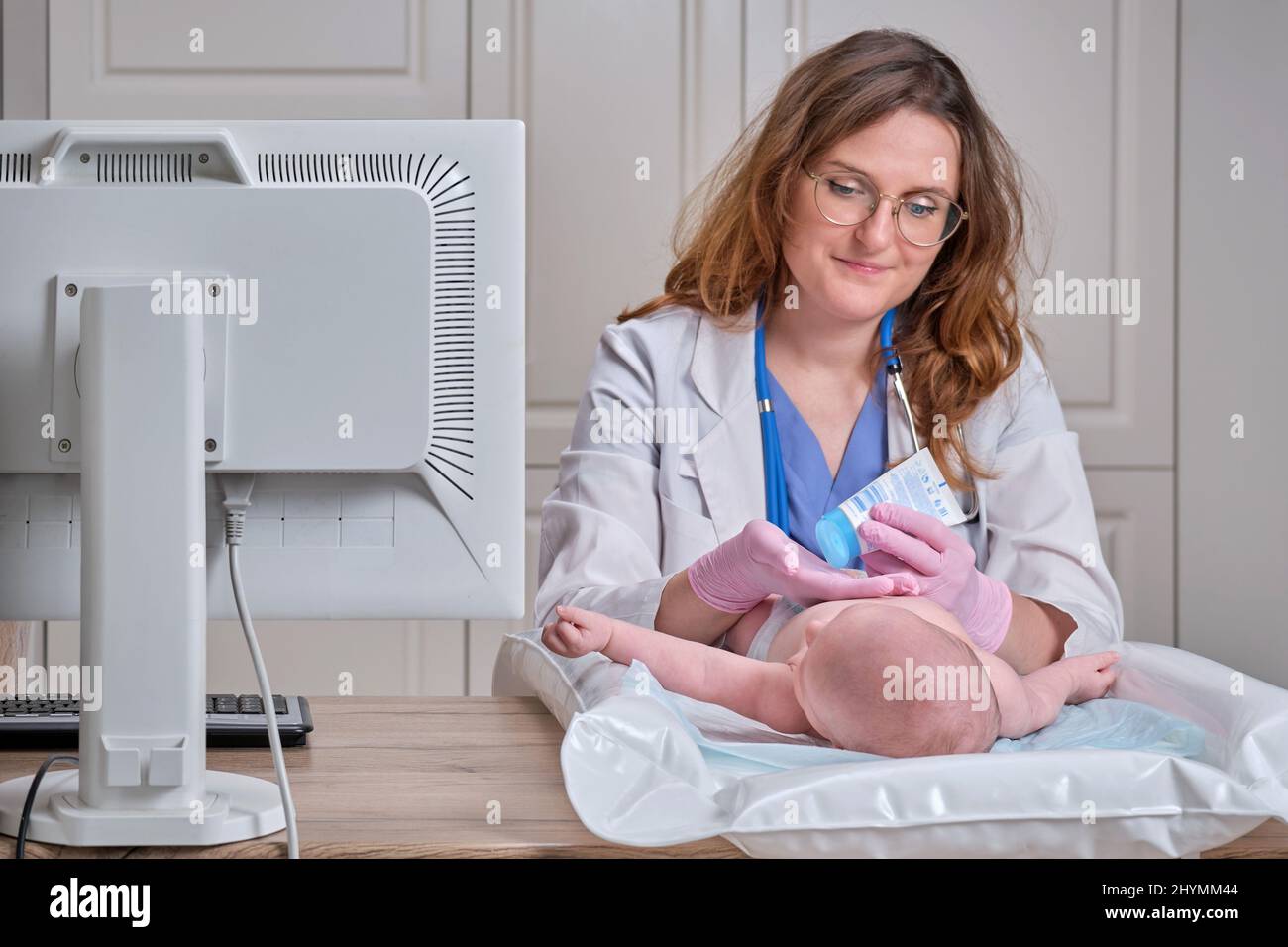 Il medico spalma una crema sulla pelle di un neonato. Infermiere dermatologo in uniforme Foto Stock