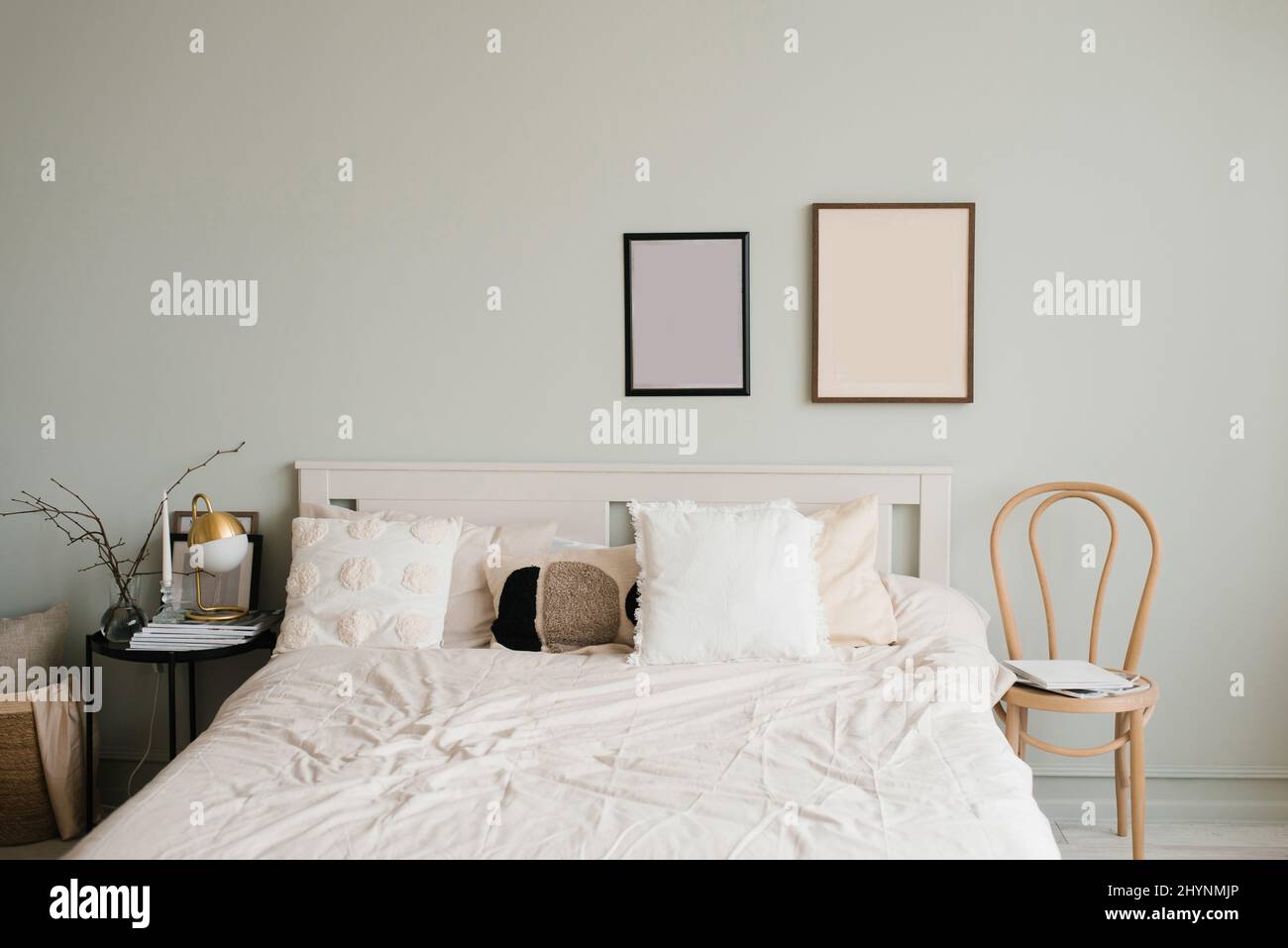 Letto matrimoniale con lenzuola bianche e cuscini beige in una luminosa camera scandinava, quadri mockup sopra il letto Foto Stock
