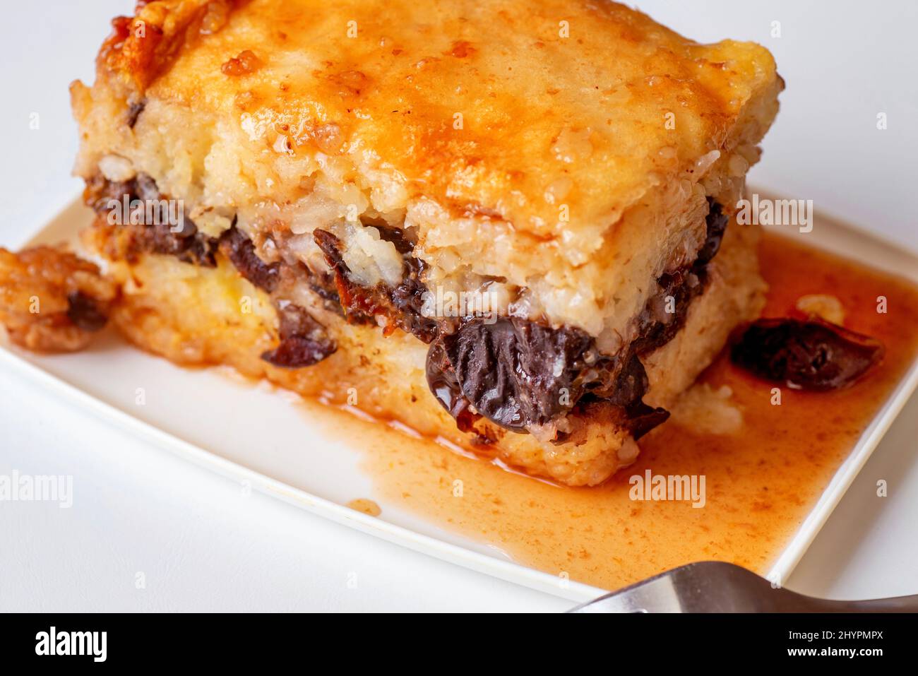 Budino di prugna di riso con salsa su piatto bianco rettangolare con forchetta su sfondo bianco, dessert sano, primo piano. Foto Stock