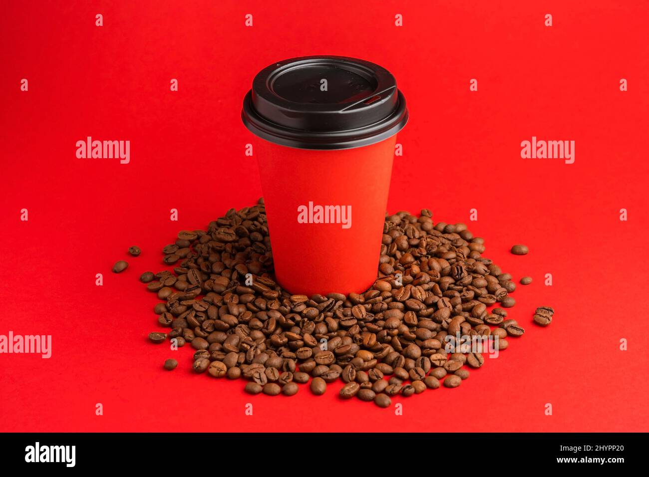 Tazza da caffè in carta rossa da asporto con tappo nero su chicchi tostati su sfondo rosso. Mock up Foto Stock