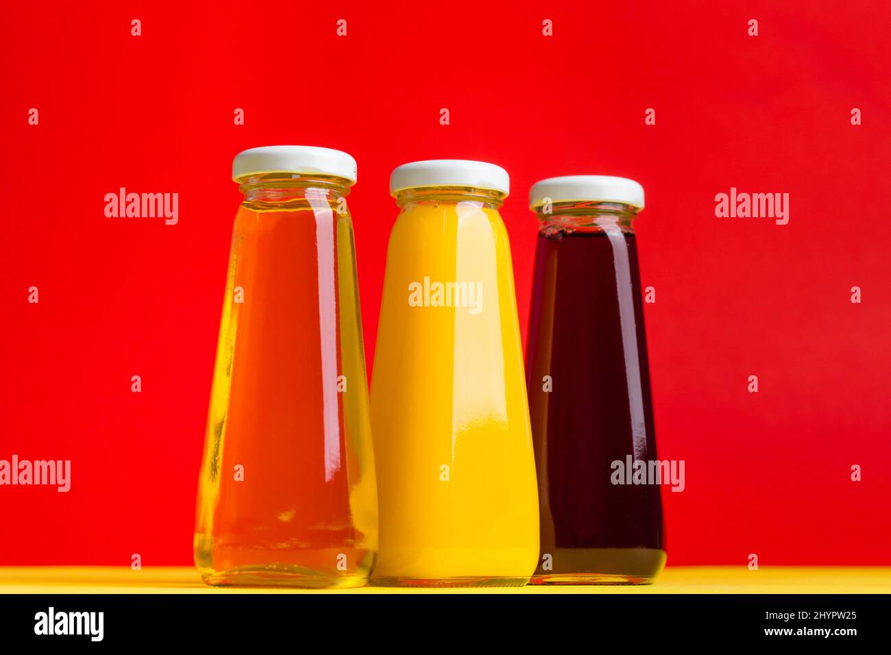 Bottiglie con bevanda a base di acqua halthy liquida gialla e rossa su sfondo giallo e rosso. Ciliegia di mela arancione Foto Stock