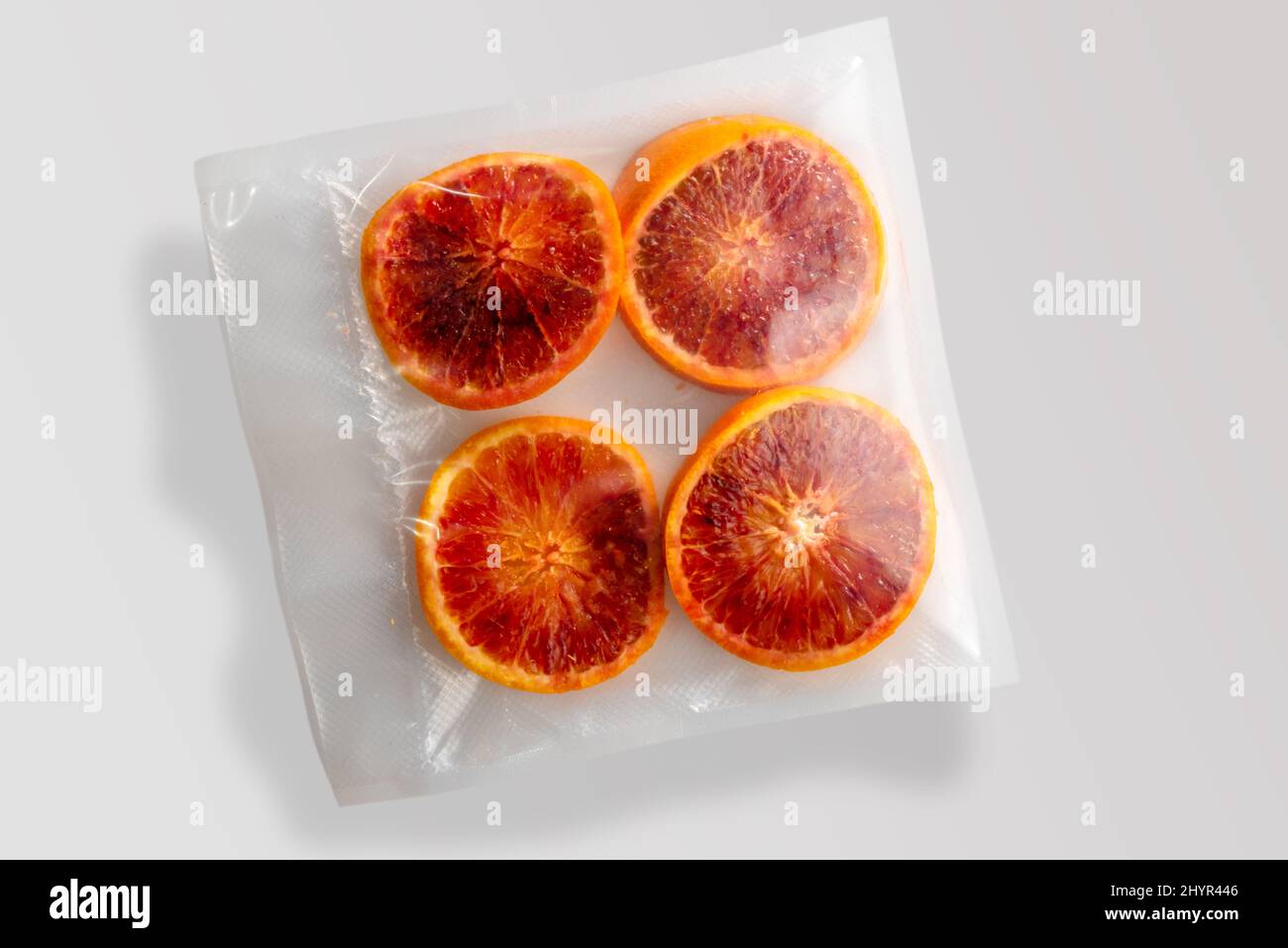 Quattro fette di frutta di arance rosse confezionate sottovuoto sigillate per una cottura sous vide isolate su sfondo grigio nella vista dall'alto Foto Stock