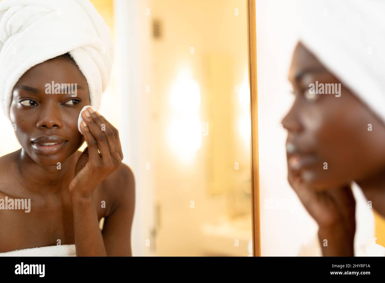 Riflesso della spugna di strofinamento della donna africana americana sul viso in bagno a casa Foto Stock