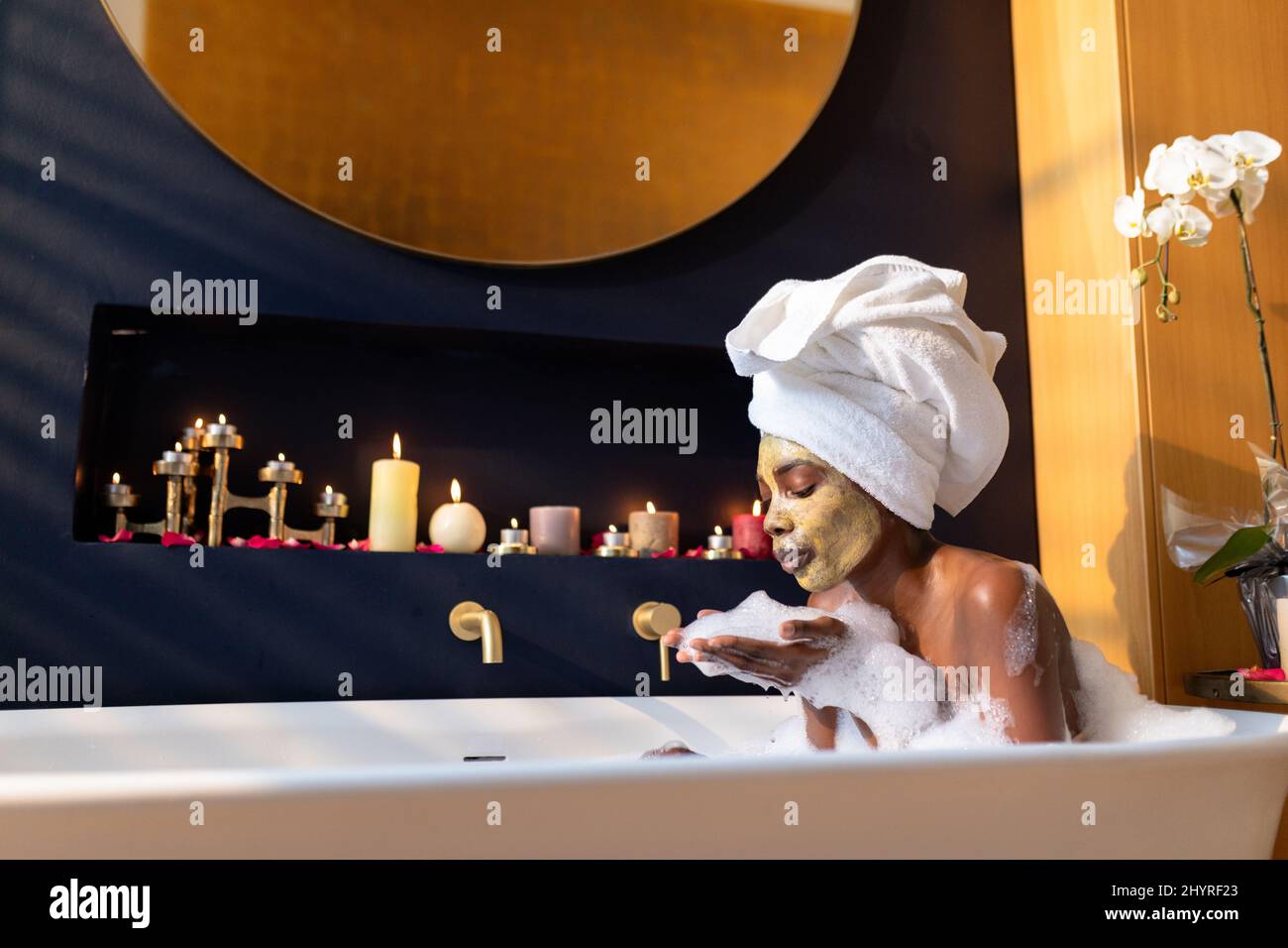 Donna afroamericana che soffia sapone sud a portata di mano mentre si rilassa nella vasca da bagno di casa Foto Stock