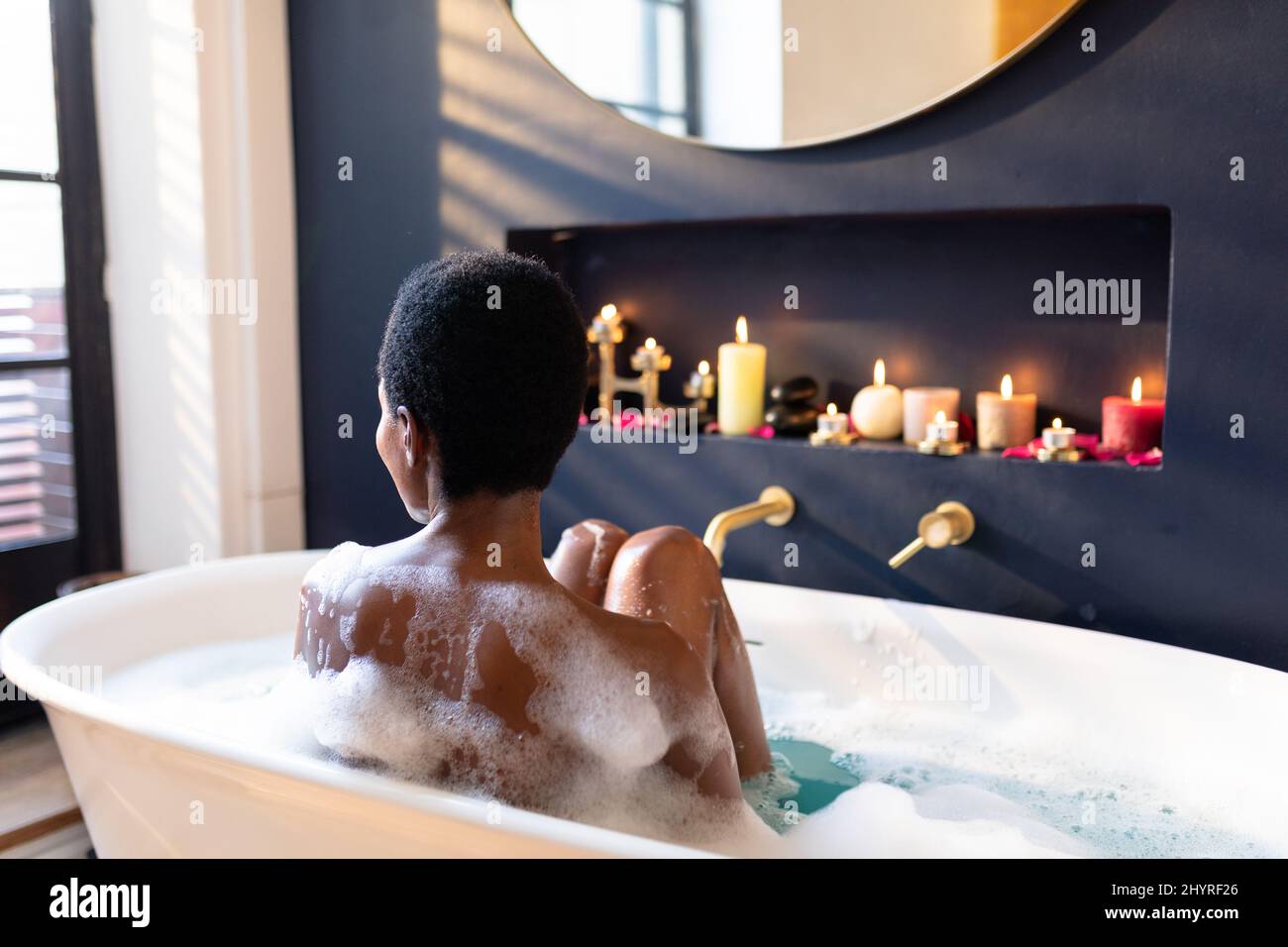 Nuda giovane afroamericana che si rilassa nella vasca da bagno mentre si guarda via a casa Foto Stock