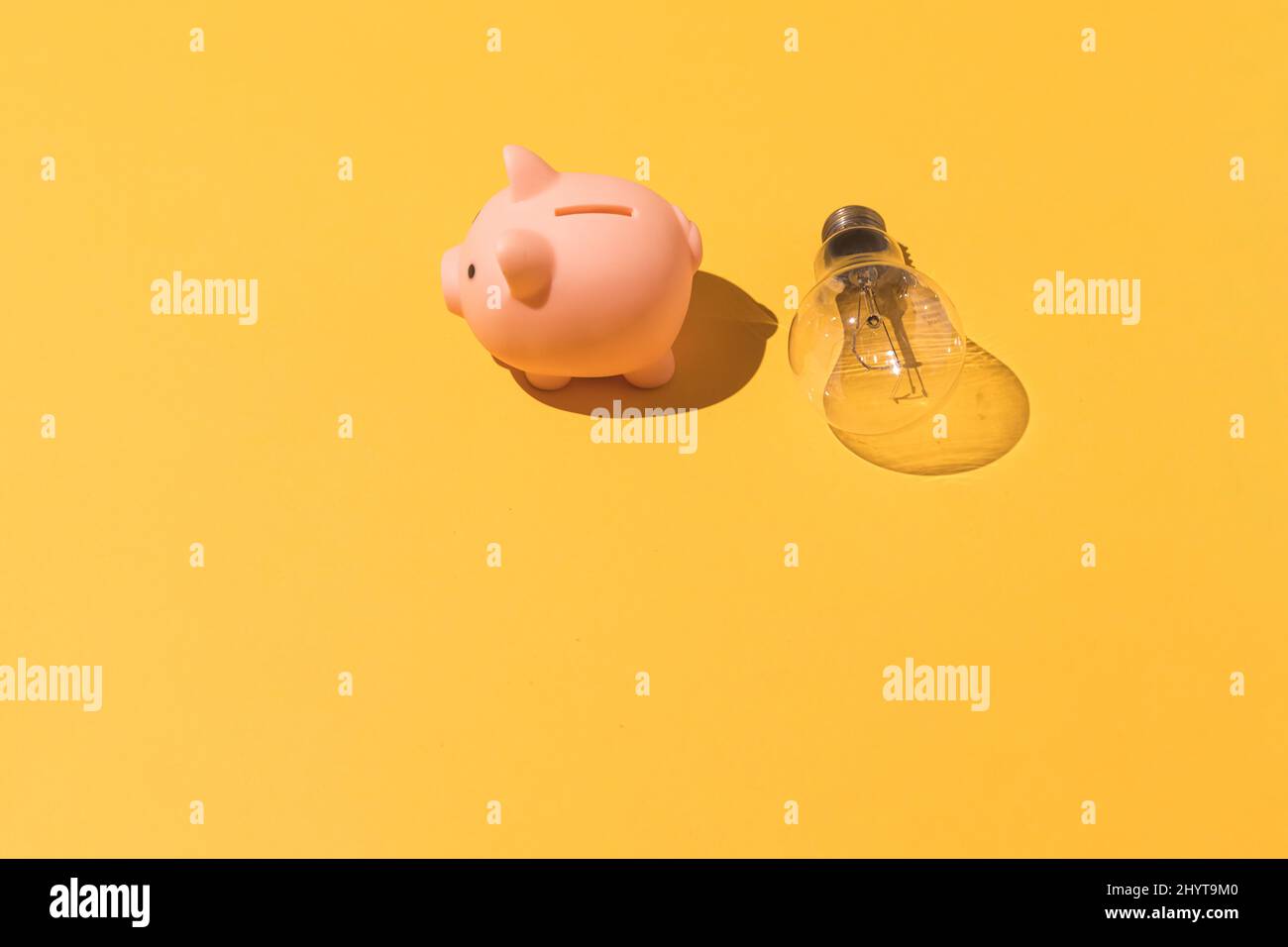 Piggy Bank e lampadina su sfondo giallo. Concetto di elettricità, aumento dei prezzi, impoverimento ed economia. Foto Stock