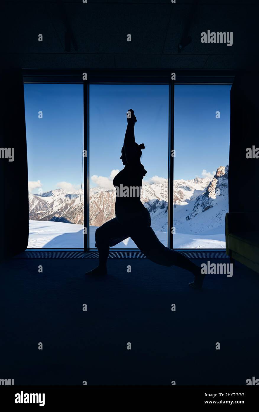 Giovane donna silhouette fare meditazione yoga guerriero virabhadrasana posa con in camera con vista panoramica di uno splendido paesaggio di montagna. Healt Foto Stock