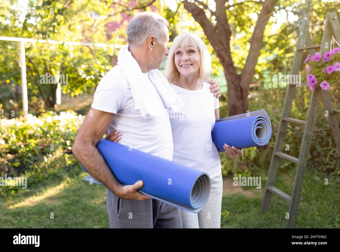 Pensionamento sano. Sposi anziani attivi e felici che tengono stuoie per yoga, pronti per l'esercizio all'aperto nel loro giardino Foto Stock