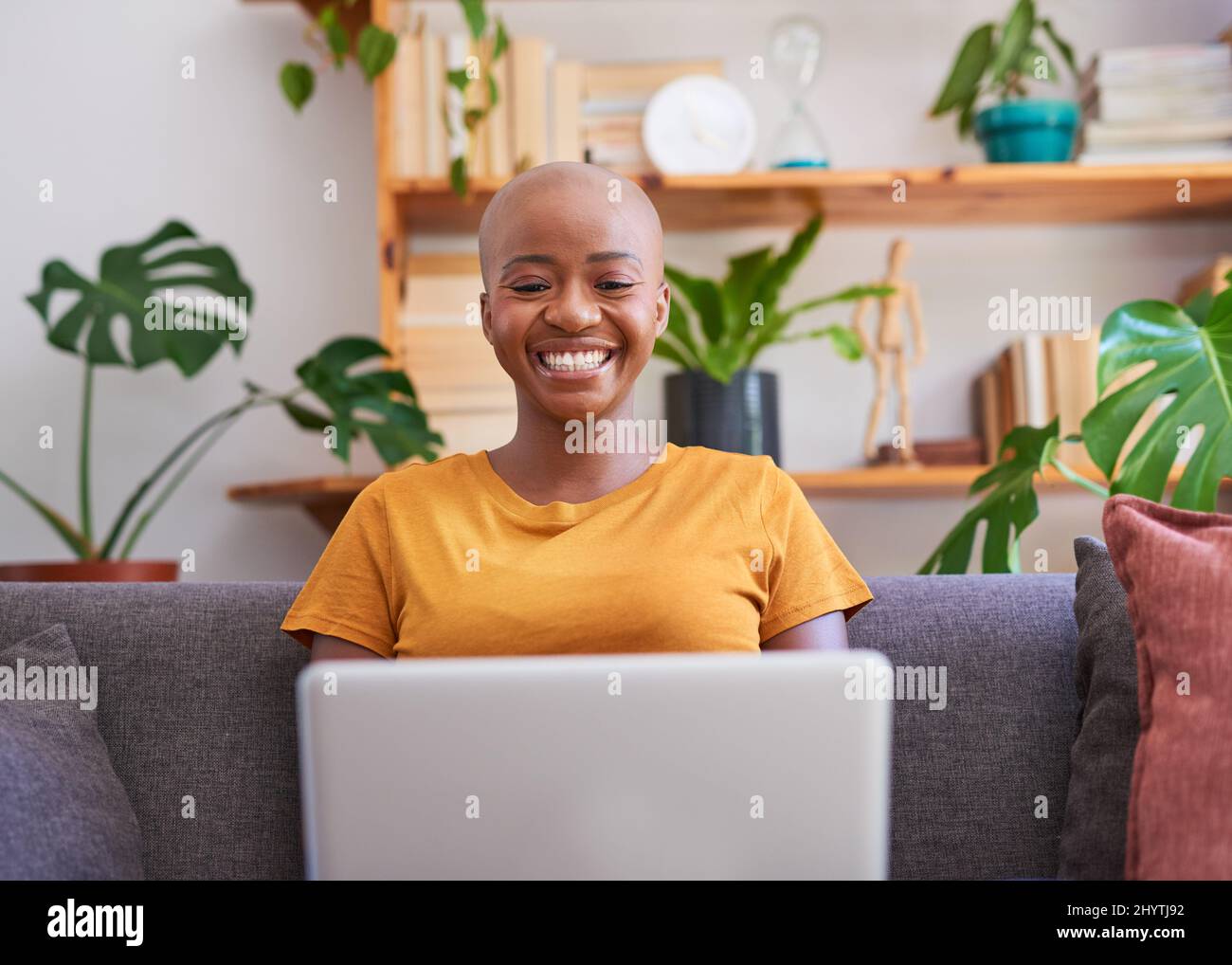 Una giovane donna si siede sul divano con il suo laptop e sorride Foto Stock
