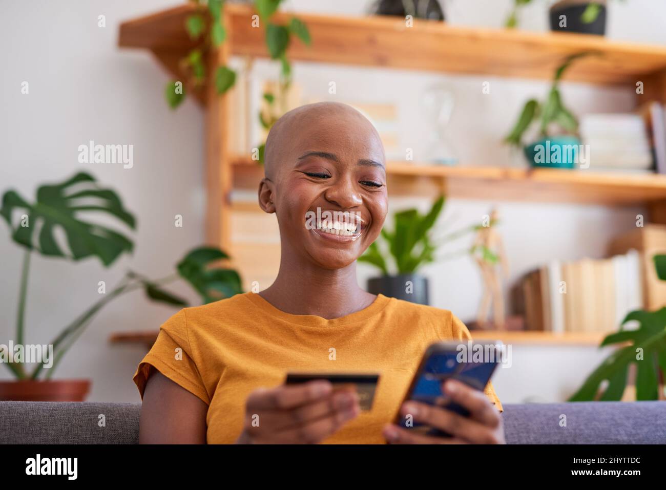 Una giovane donna tiene una carta di credito e negozi online dal suo divano soggiorno Foto Stock