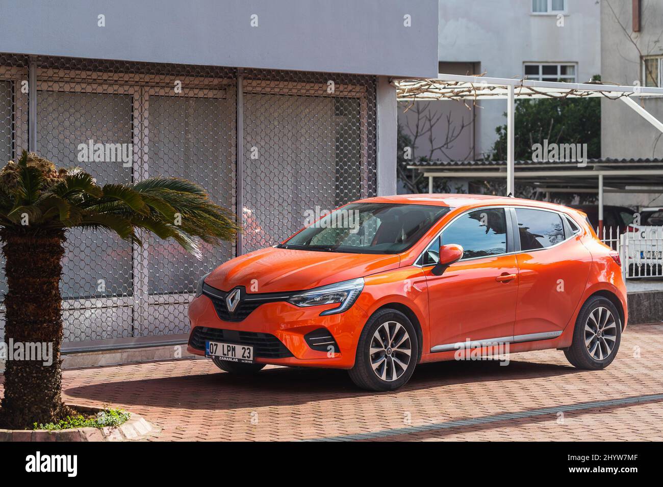 Side; Turchia – Febbraio 20 2022: Orange Renault Clio è parcheggiata in strada in una calda giornata estiva sullo sfondo di un negozio Foto Stock