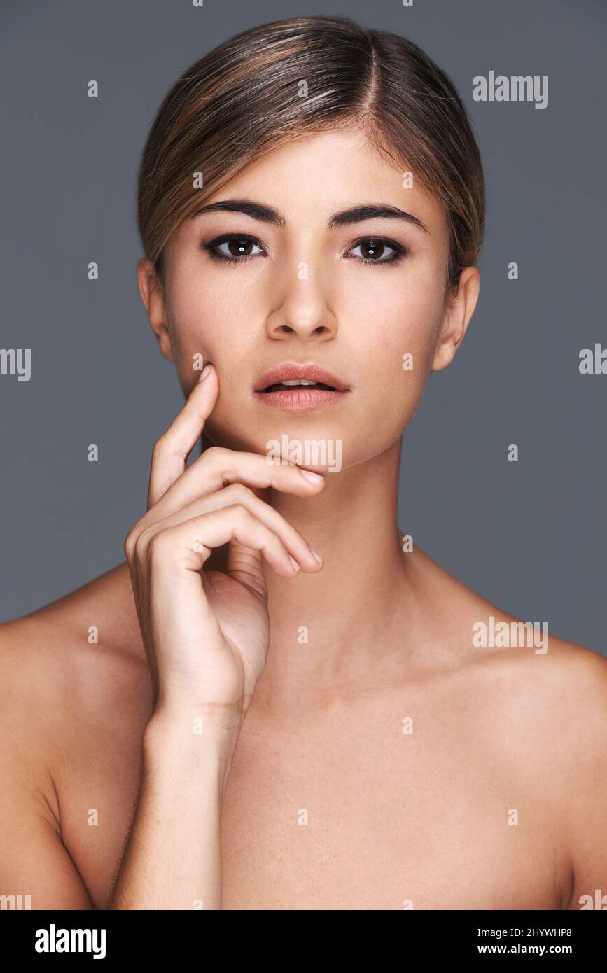 Pelle incredibilmente morbida. Un ritratto corto di una bella giovane donna che toching il suo volto isolato su grigio. Foto Stock