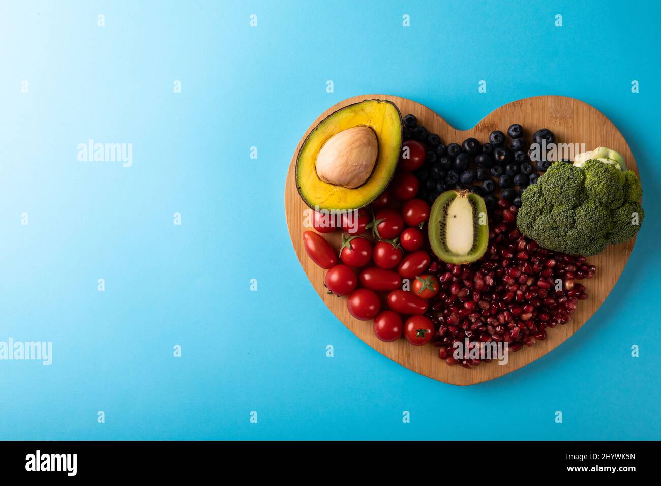 Direttamente sopra la vista di cibo sano su bordo di taglio a forma di cuore su sfondo blu Foto Stock