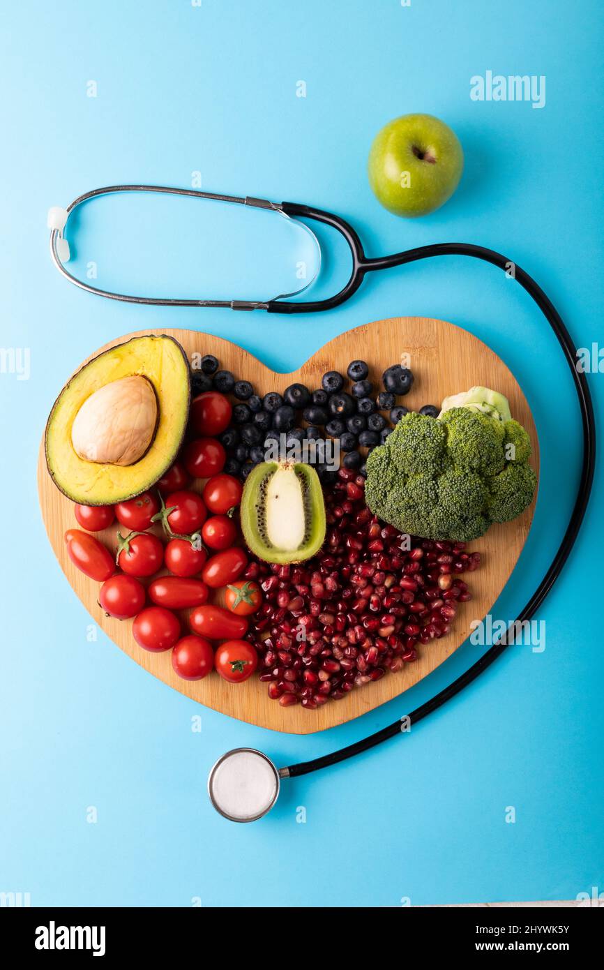 Direttamente sopra la vista di cibo sano su tagliere a forma di cuore da stetoscopio su sfondo blu Foto Stock