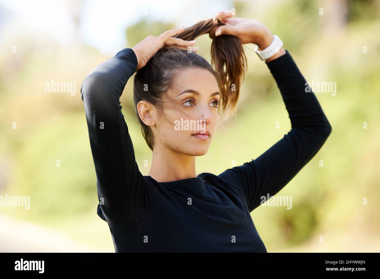 Assicurandosi che i suoi capelli doesnt ottengono nel senso. Scatto corto di una giovane donna atletica e attraente che lega i suoi capelli indietro mentre si levano in piedi all'aperto. Foto Stock
