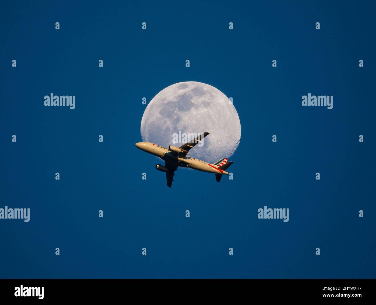 Un jet passeggeri American Airlines passa davanti alla luna piena al tramonto poco dopo il decollo dall'aeroporto internazionale Charlotte-Douglas di Charlo Foto Stock