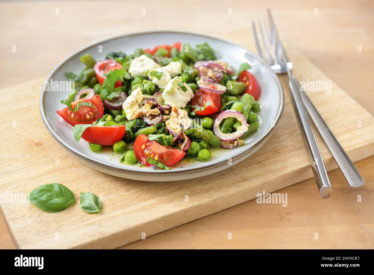 Piatto sano da verdure verdi come piselli, fagioli e spinaci con cipolle brasate, formaggio feta e pomodori per una dieta vegetariana a basso contenuto di carb, copia spa Foto Stock
