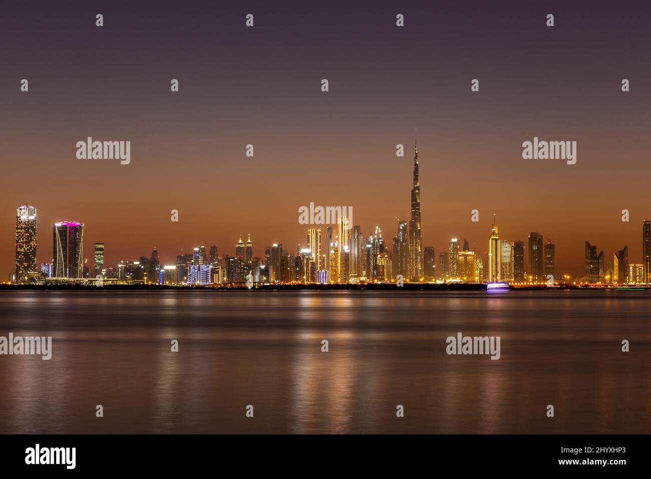 Lo skyline della Dubai Business Bay di notte con edifici colorati illuminati e la calma acqua del Dubai Creek. Foto Stock