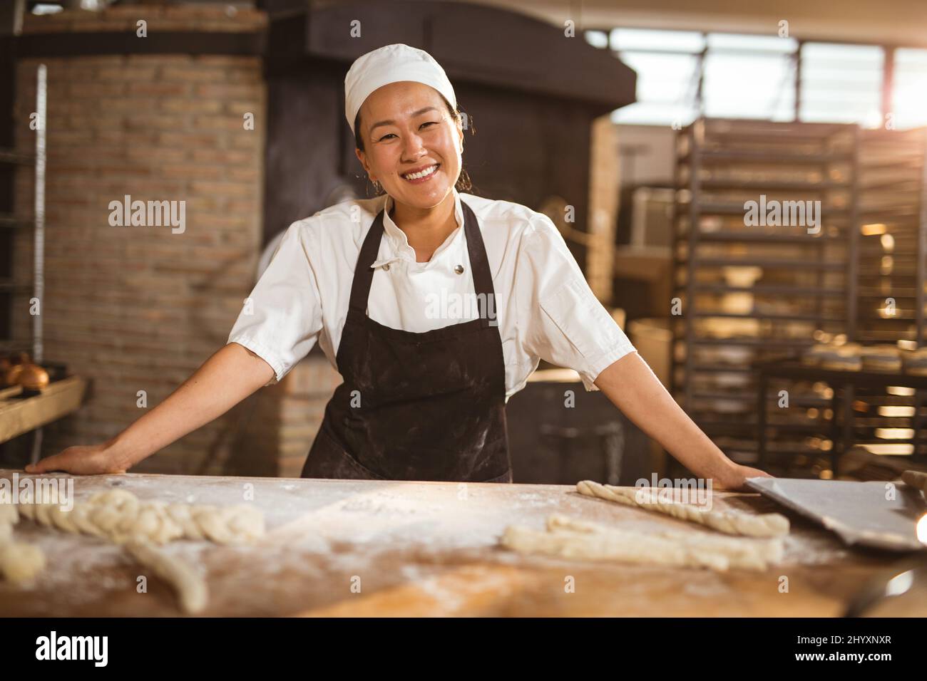 Ritratto di sorridente asiatico metà adulta donna panettiere in piedi in panetteria Foto Stock