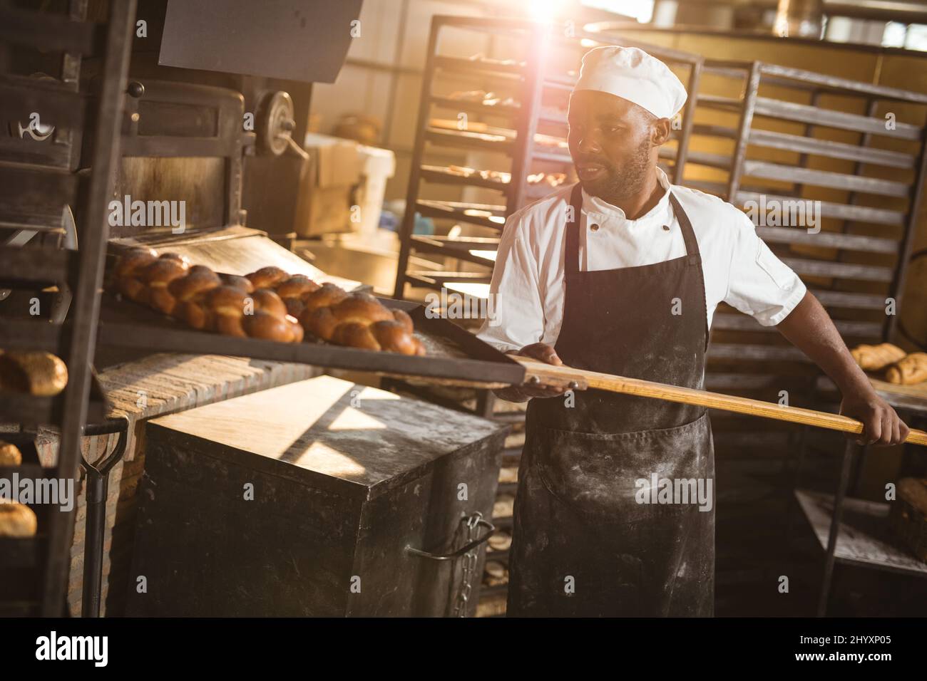 African american MID adult maschio panettiere mantenere intrecciato vassoio del pane con lunga spatola in rack Foto Stock