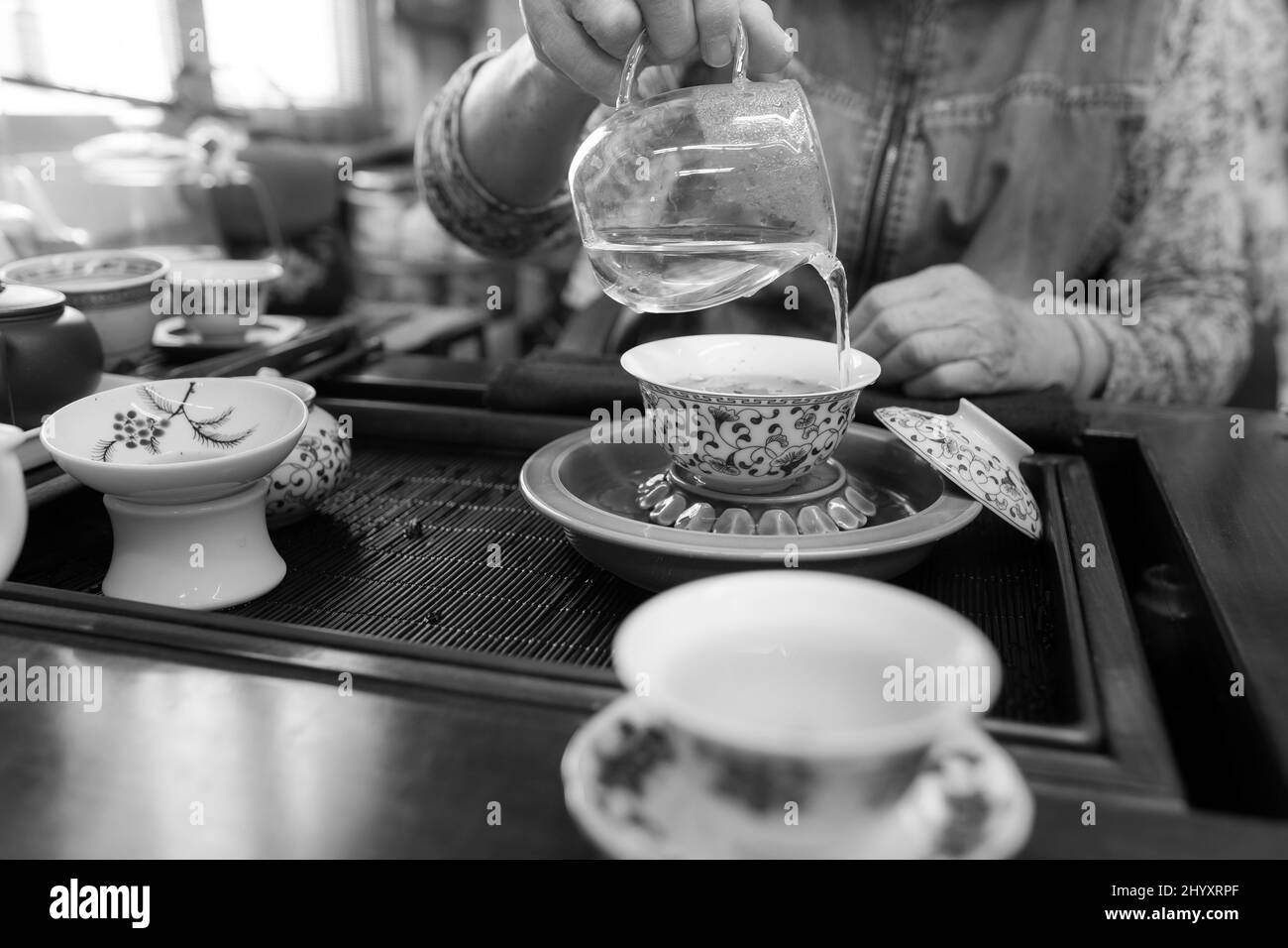 Gong fu Cha che produce birra utilizzando un gaiwan di porcellana e una tazza di giustizia/giustizia in vetro. Tradizionale metodo di bere tè cinese. Gennaio 2020. Bianco e nero Foto Stock