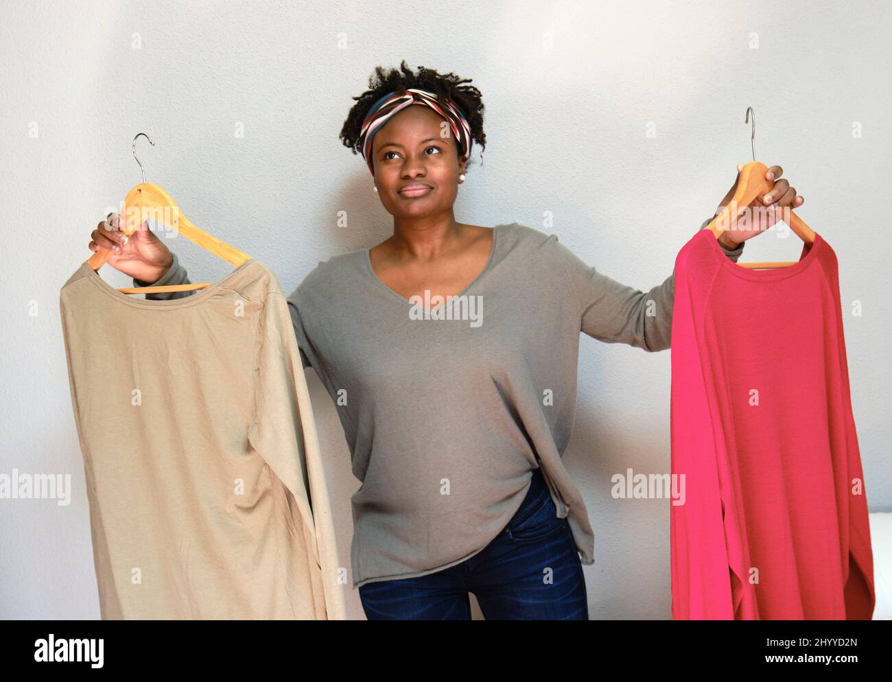 Ritratto di giovane donna nera con acconciatura afro con abiti su appendiabiti interni a casa. Concetto di stile di vita. Foto Stock
