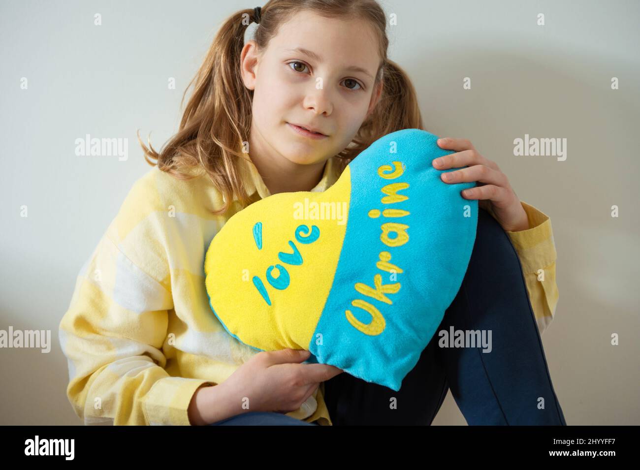 Ragazza adolescente carina seduta sul pavimento e tenendo un cuscino di colori bandiera ucraini Foto Stock