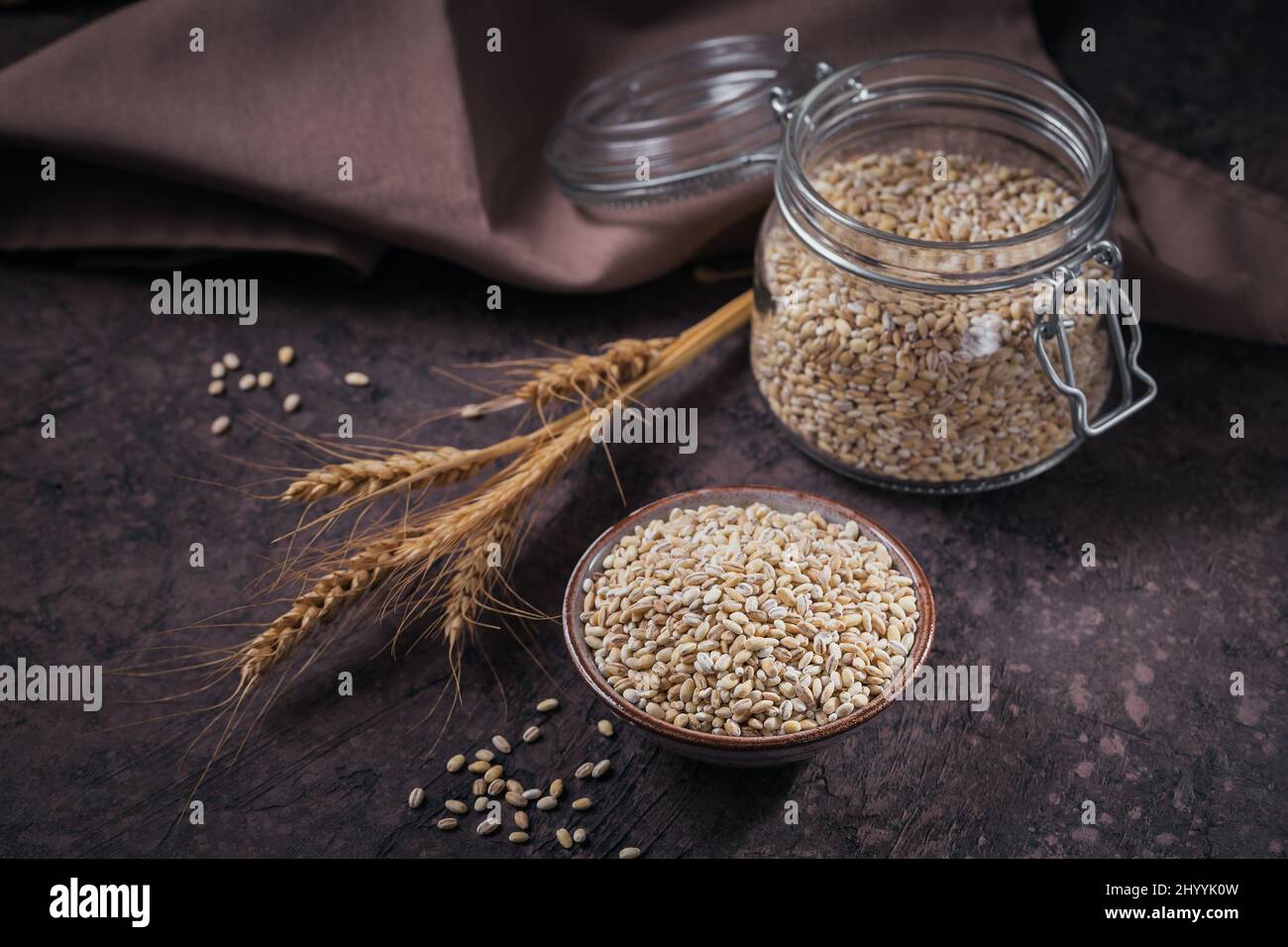 Ciotola di grano crudo secco di orzo perlato rotto su fondo scuro. Cucina Perla orzo porridge concetto. Foto Stock