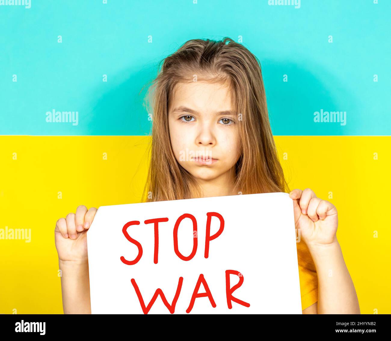Una ragazza sta piangendo, tenendo in mano un manifesto DI FINE GUERRA contro lo sfondo della bandiera Ucraina. Foto Stock