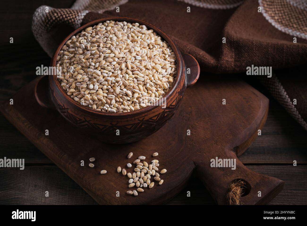 Ciotola di grano crudo secco di orzo perlato rotto su fondo di legno scuro. Cucina Perla orzo porridge concetto. Foto Stock