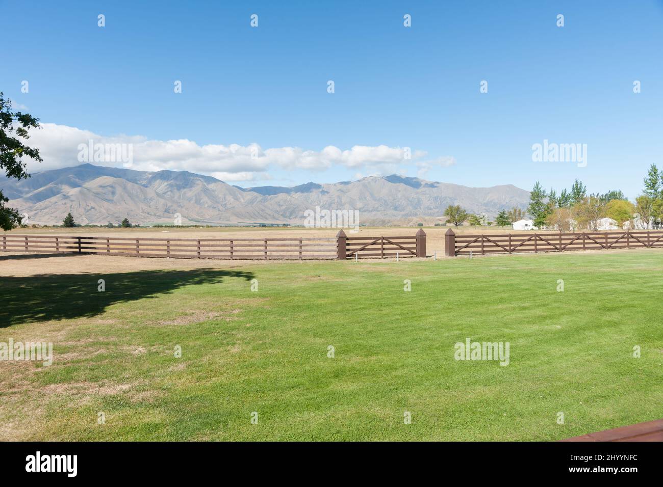 Campo verde e recinto di legno marrone in vista delle montagne circostanti a Omarama South Island, Nuova Zelanda. Foto Stock