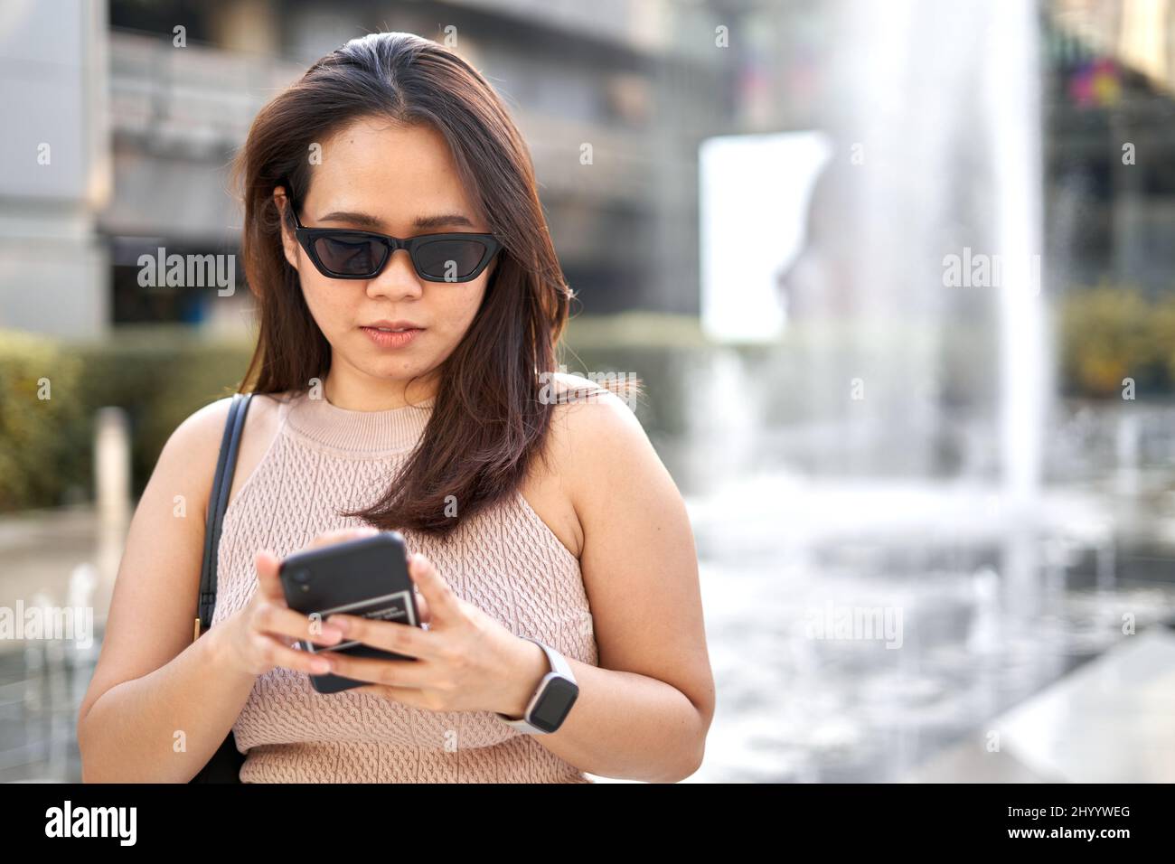 Ritratto di una donna asiatica che usa il mobile mentre indossa occhiali da sole all'aperto Foto Stock