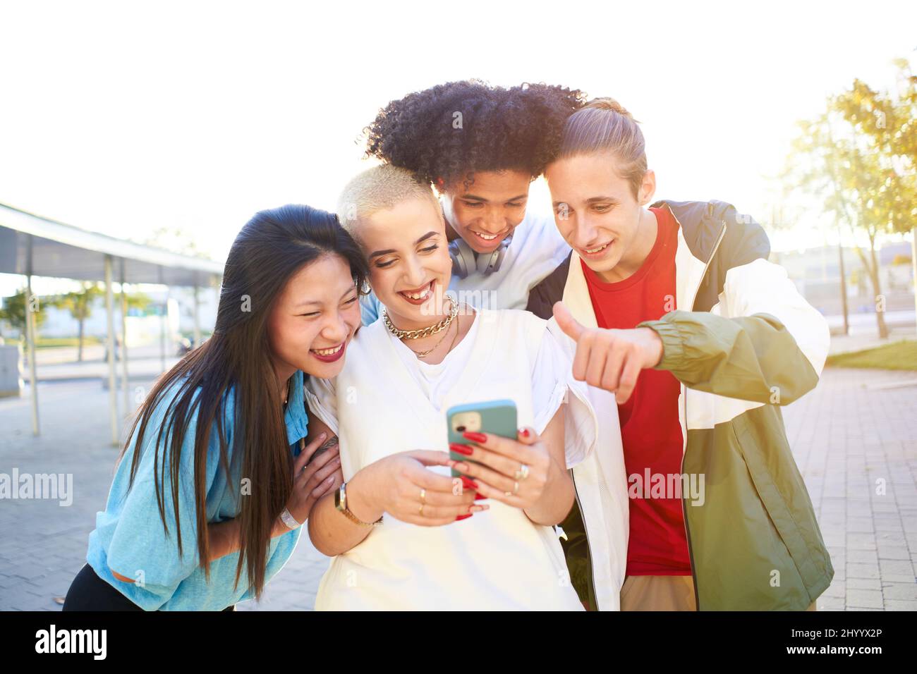Gruppo di amici felici con il telefono e divertirsi in strada. Ragazzi che condividono con cellulare in videochiamata Foto Stock