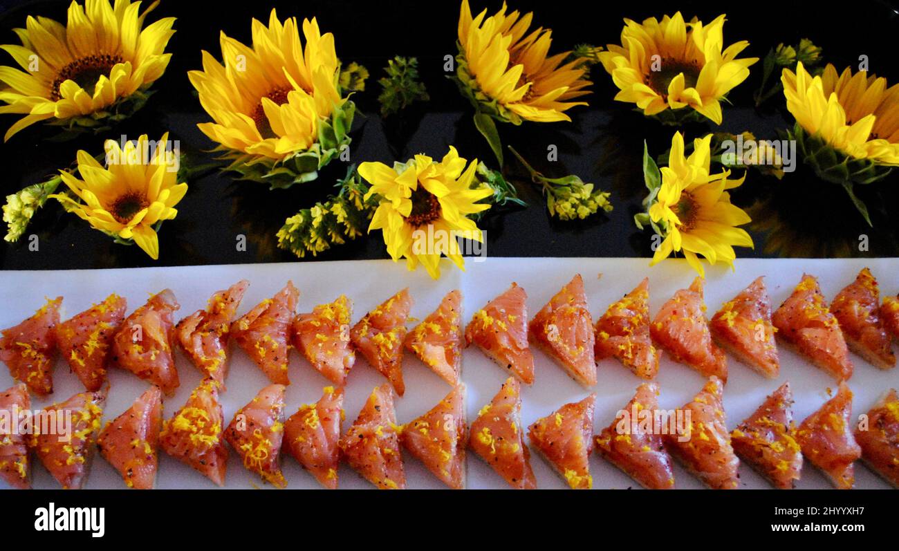 Canapé di salmone affumicato cocktail hors d'oeuvre su tovagliolo bianco su vassoio decorato con girasoli. Foto Stock