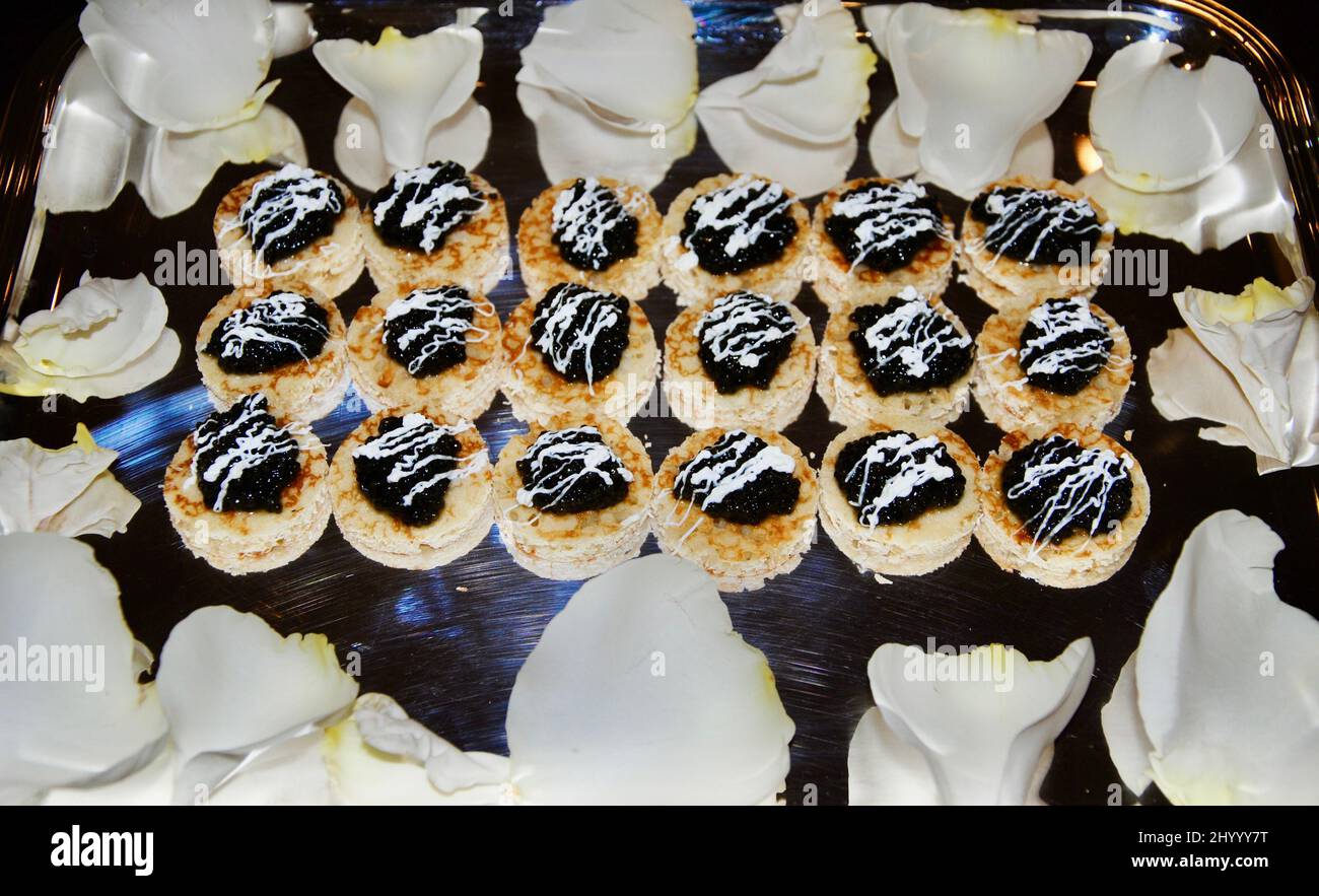Caviale nero su piccolo cocktail blini hors d'oeuvre su vassoio decorato con petali di rosa bianchi Foto Stock