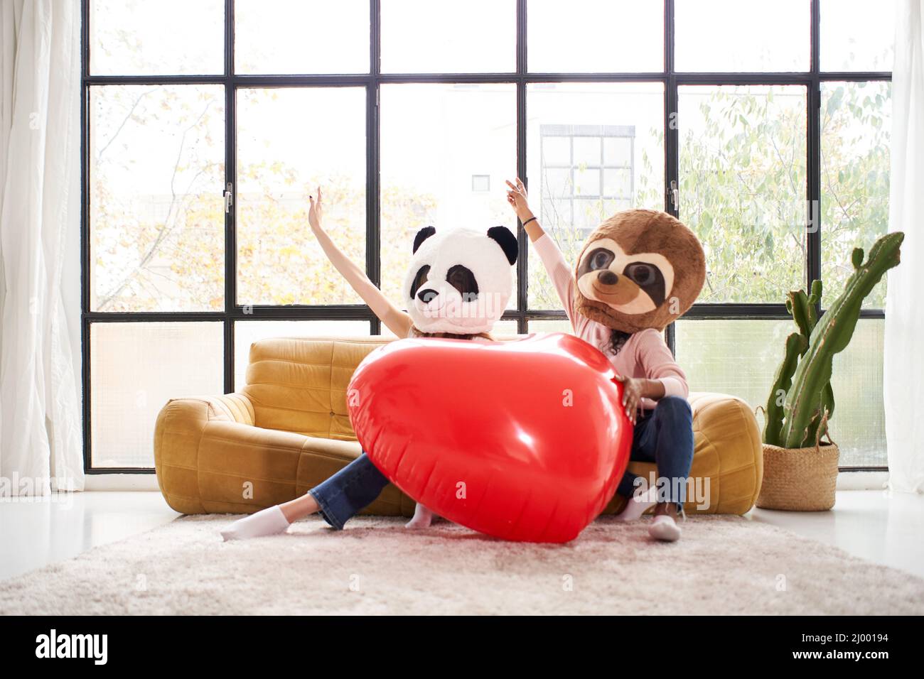 Divertente donne che indossano maschera animale orso panda tenendo grande cuore a casa - felice emozioni positive persone insieme nell'amore Foto Stock
