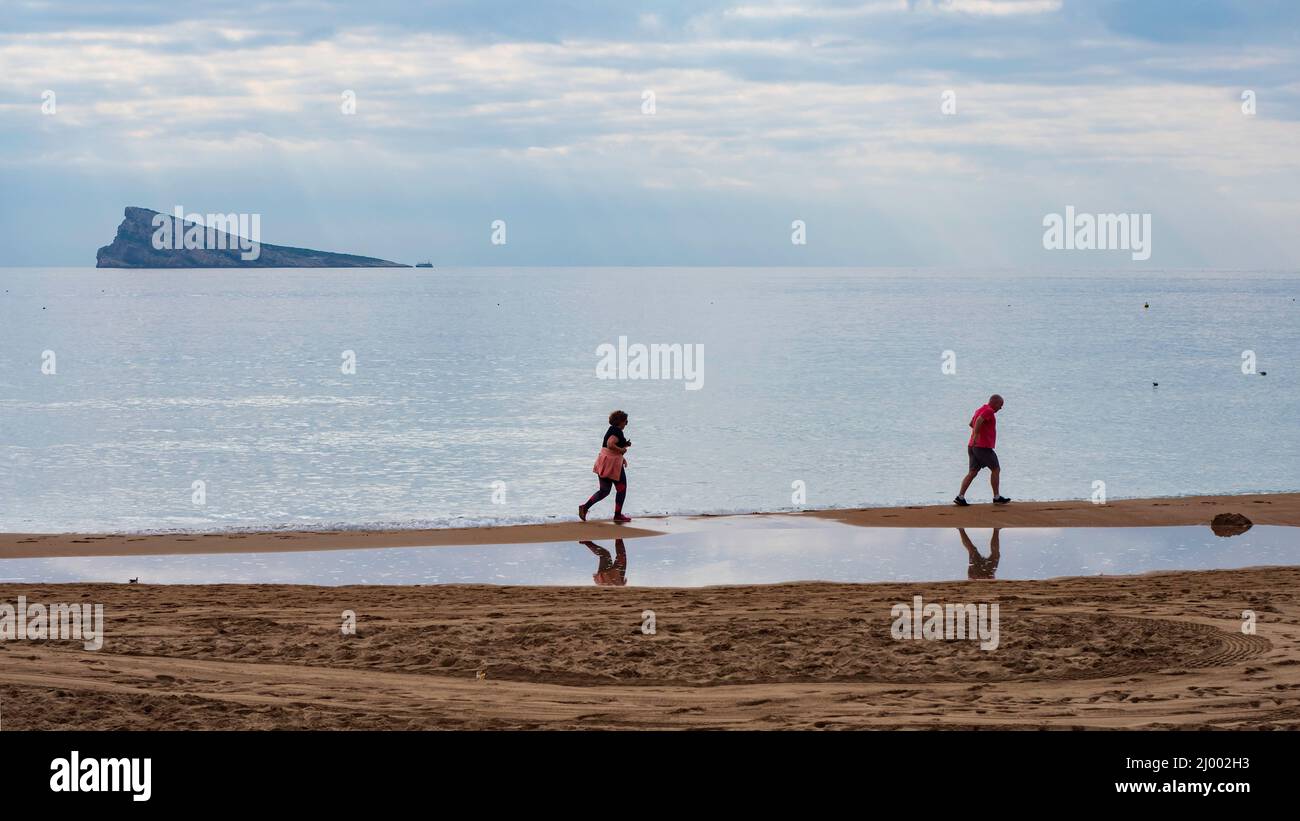 Gruppo di pensionati che camminano sulla sabbia della spiaggia di fronte al mare a Benidorm al tramonto. Foto Stock