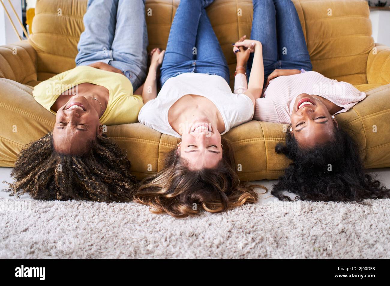 Tre fidanzate donne felici sorridendo a divano ridere bene. I giovani che si divertono insieme a casa. Foto Stock