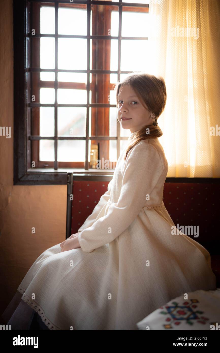 Bambina bionda in abito bianco vintage seduto all'interno di una cabina di campagna Foto Stock