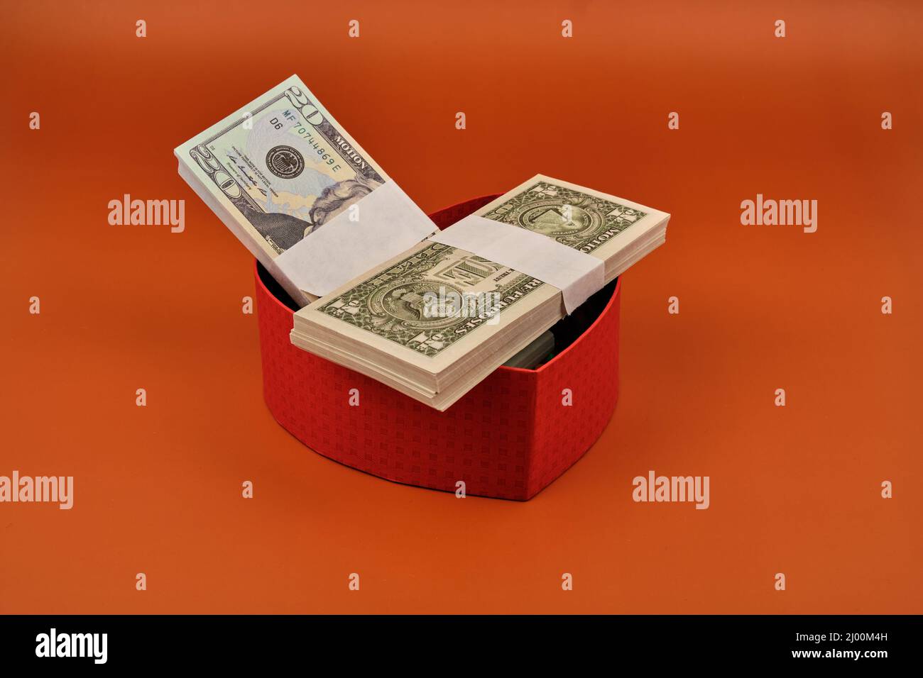 Regalo a forma di cuore pieno di dollari con sfondo arancione. Foto Stock