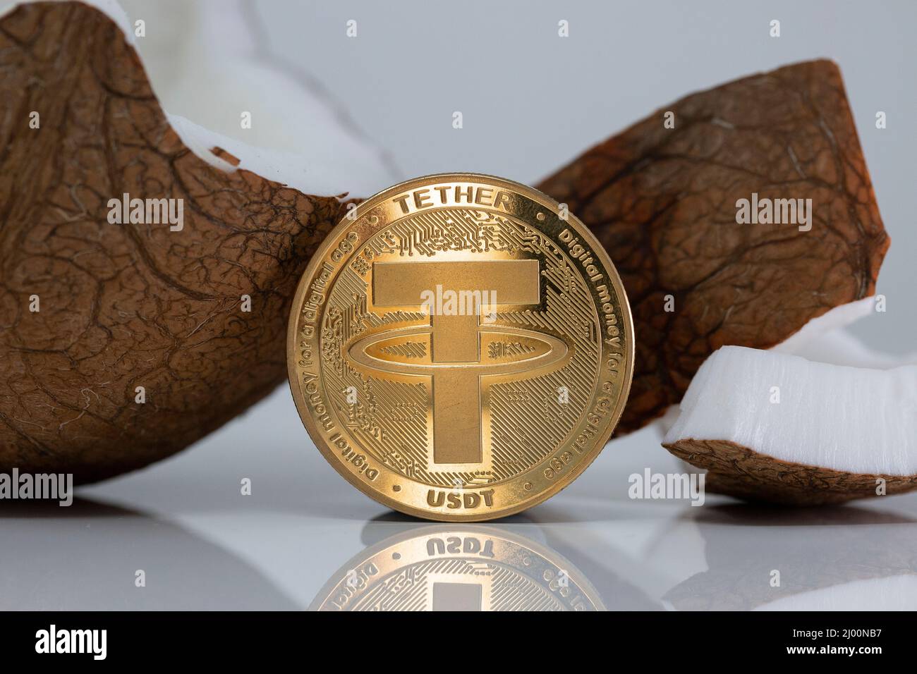 Modulo di raccordo USDT criptovaluta moneta fisica posto accanto a cocco rotto sul tavolo bianco riflettente. Scatto macro. Foto Stock