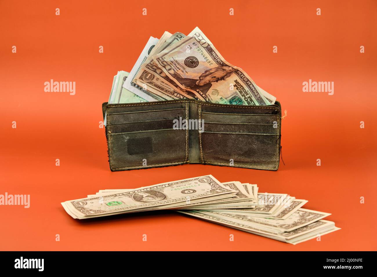 Portafoglio in pelle pieno di banconote in denaro su sfondo arancione. Concetto dell'importanza del risparmio. Foto Stock