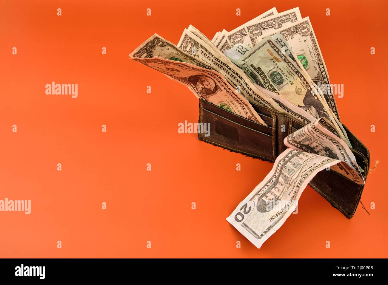 Portafoglio in pelle pieno di banconote in denaro su sfondo arancione. Concetto dell'importanza del risparmio. Foto Stock