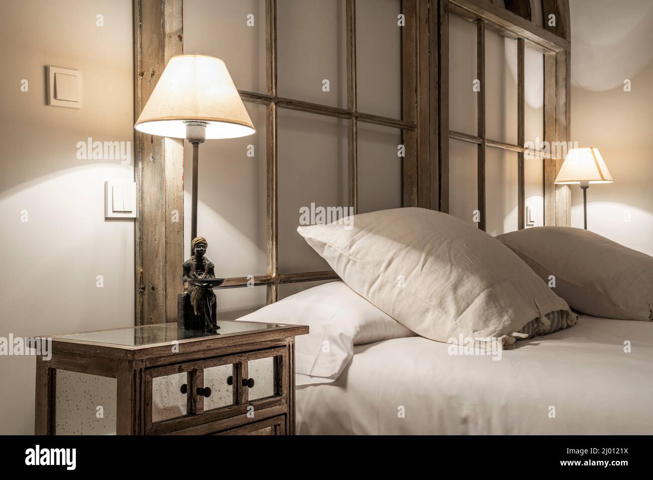 Testata di una camera da letto con letti matrimoniali con cuscini quadrati  decorati con barre di legno e comodino in vetro con lampada con piedino  decorativo Foto stock - Alamy