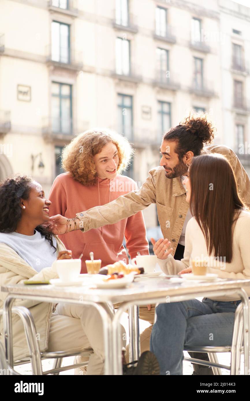 Foto verticale dei giovani che mangiano a colazione - amici felici che ridono insieme che parlano il caffè durante l'happy hour al bar ristorante caffetteria. Cibo Foto Stock
