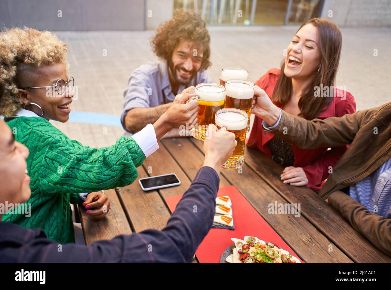 Gruppo di amici felici che tostano con la birra mentre pranzano all'aperto. L'attenzione è rivolta alle birre Foto Stock