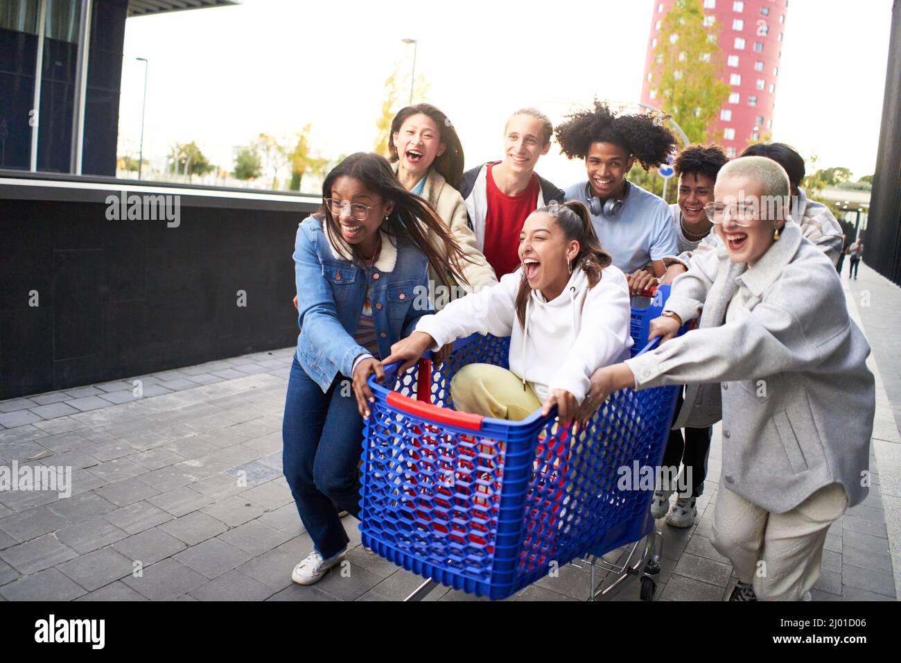 Giovani multirazziali che si divertono insieme al carrello della spesa. Amici millenari che condividono il loro tempo con i tram nel parcheggio del centro commerciale. Giovani Foto Stock