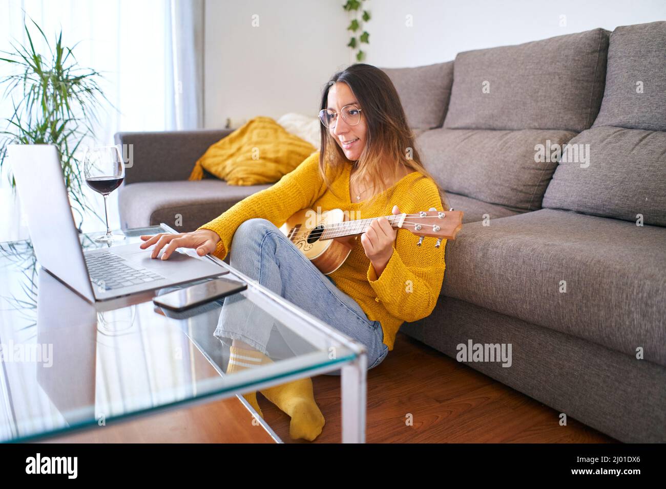 Donna che prende lezioni di ukulele online dal suo laptop durante la quarantena covid. Foto Stock